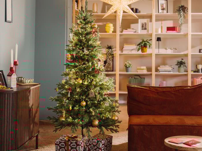 Jodła Nordmanna, sztuczna choinka FairyTrees FT05, stoi pięknie ubrana w salonie małego mieszkania podczas zimowego wieczoru.
