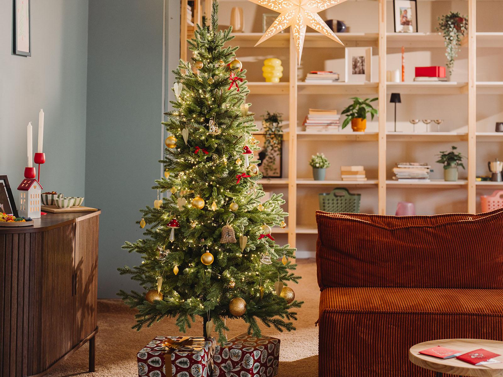 Jodła Nordmanna, sztuczna choinka FairyTrees FT05, stoi pięknie ubrana w salonie małego mieszkania podczas zimowego wieczoru.