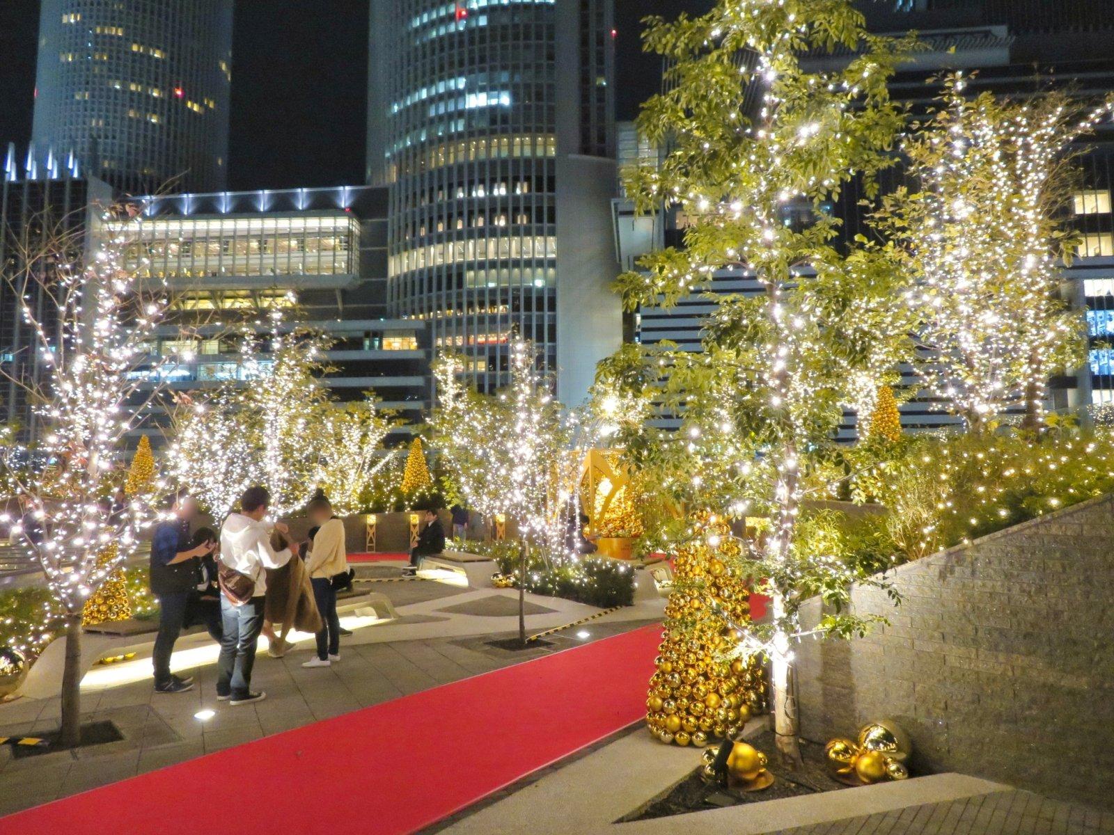 Taras na dachu budynku Dai-Nagoya w Tokio ozdobiony świątecznymi iluminacjami i choinkami, pośr&oacute;d nowoczesnej zabudowy miasta.