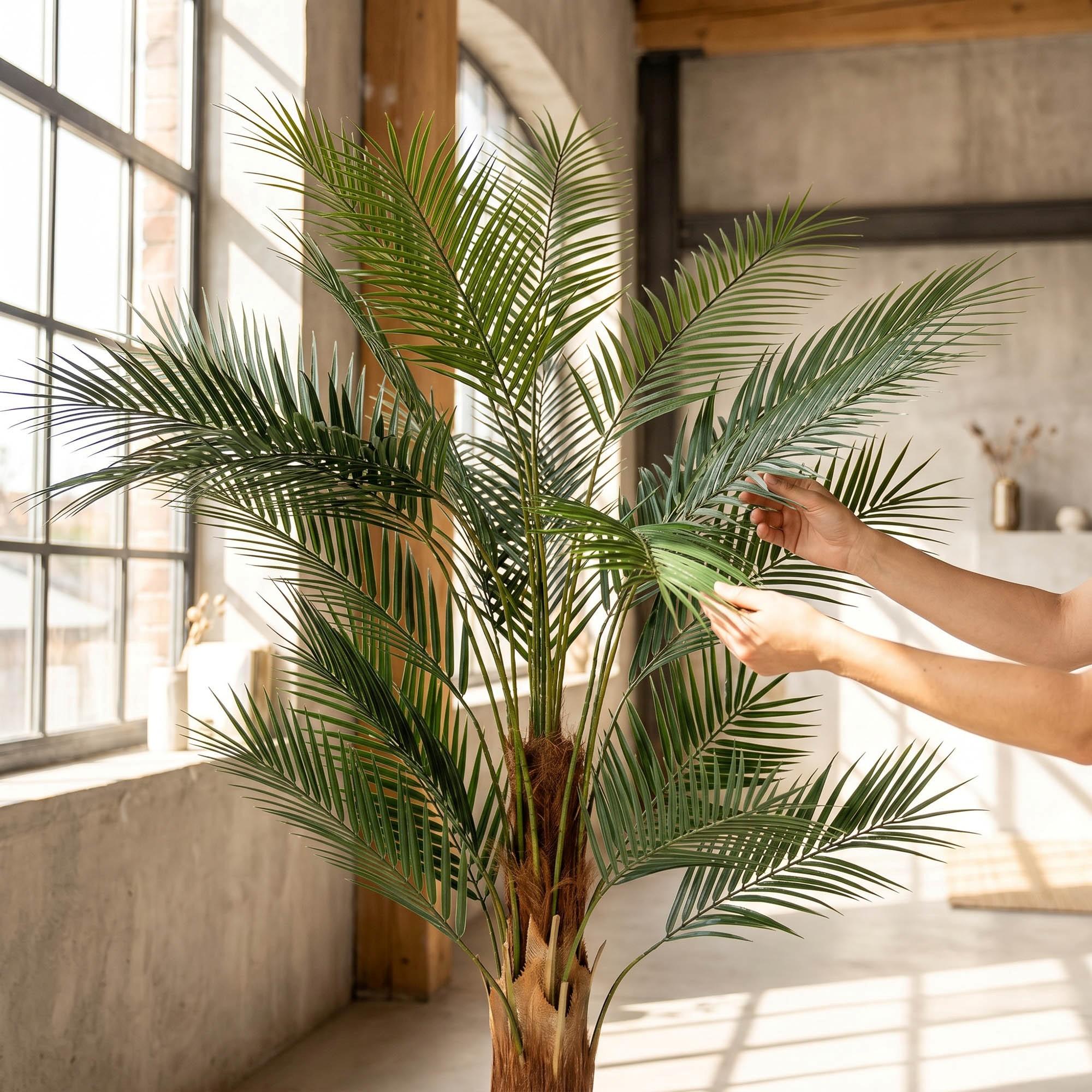 Dłonie poprawiają liście sztucznej monstery na pniu 160 cm FairyTrees, podkreślając ich naturalny wygląd i elastyczność.
